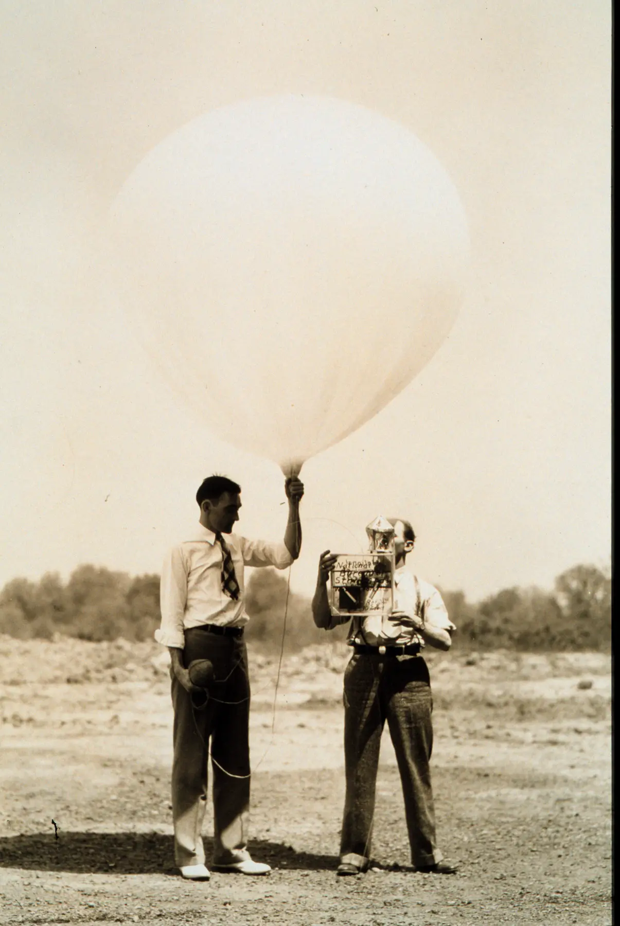 1936 photograph: two men prepare an early radiosonde, one holding up a large balloon, the other an instrument box